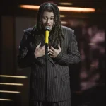 Sanremo 2026 – Sayf contailleur doppio petto rigato marrone, con cravatta di pelle.