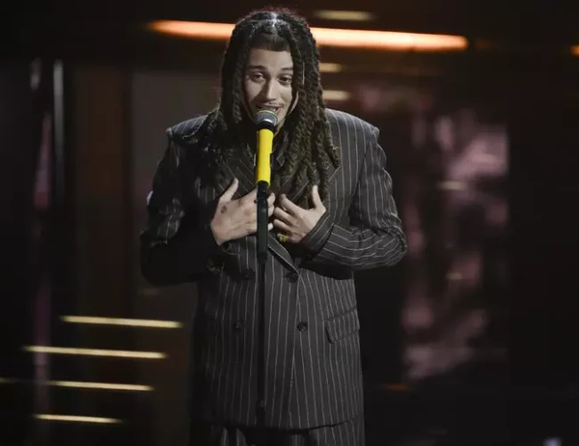 Sanremo 2026 – Sayf contailleur doppio petto rigato marrone, con cravatta di pelle.